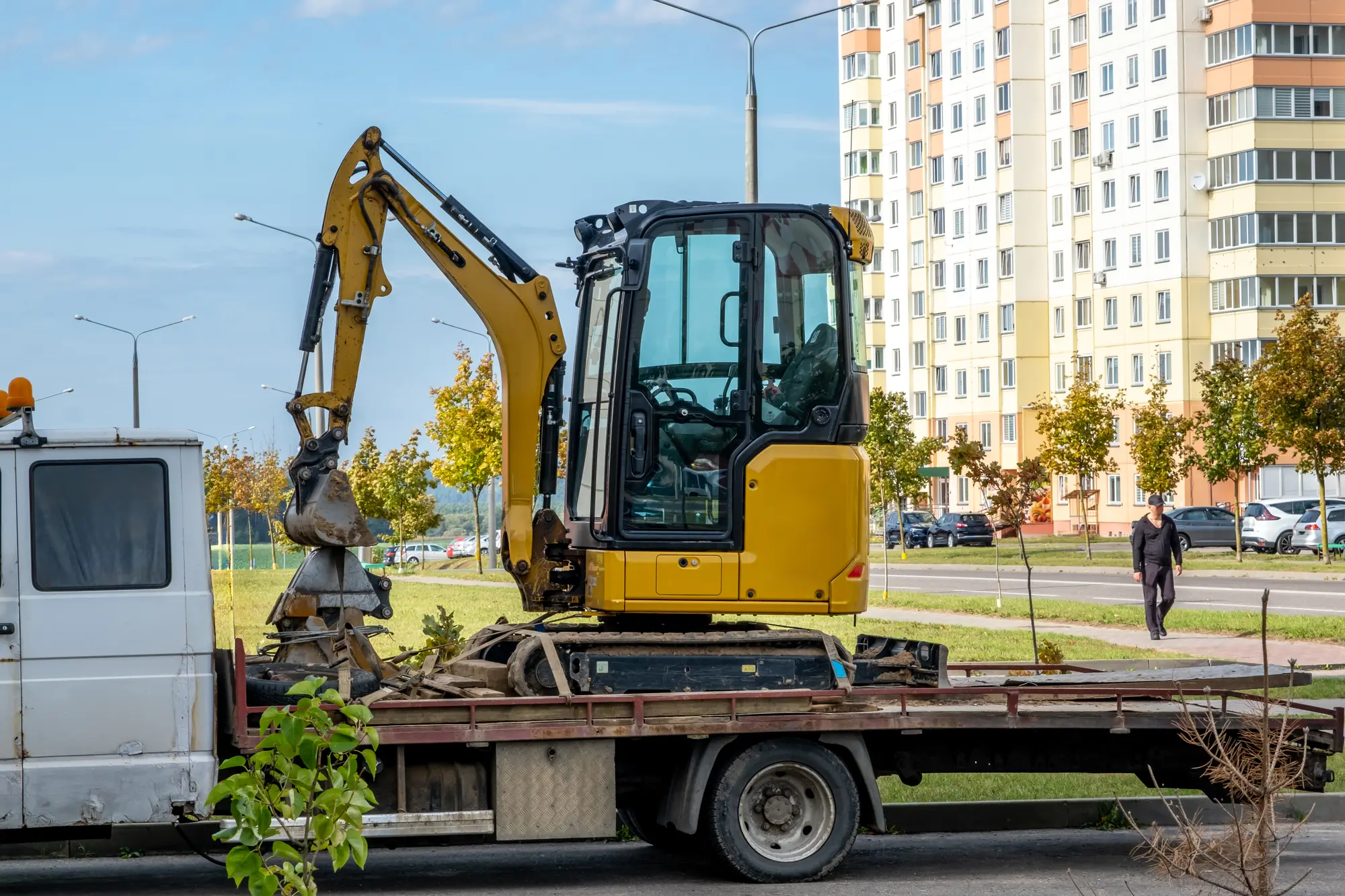 Minikoparka zamocowana na platformie lawety na osiedlowej ulicy